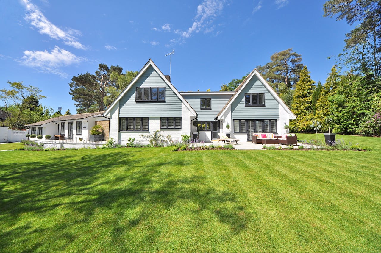 heros-img Modern family home exterior showcasing a large lawn and garden under a clear blue sky.